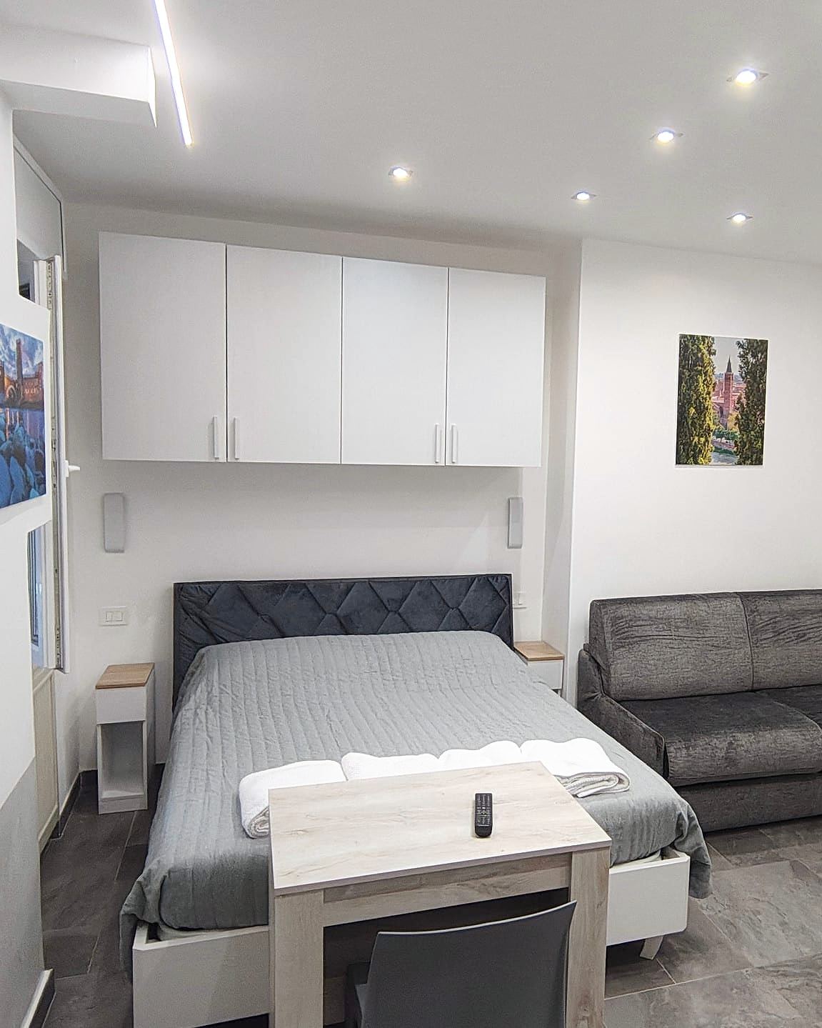 Letto matrimoniale con testiera trapuntata grigio-blu, comodini con piano in rovere e pensili bianchi