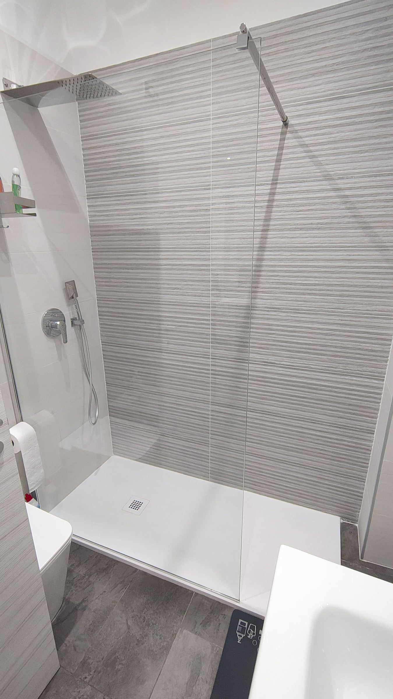 Doccia walk-in con vetro trasparente e parete di fondo in piastrelle grigie a righe