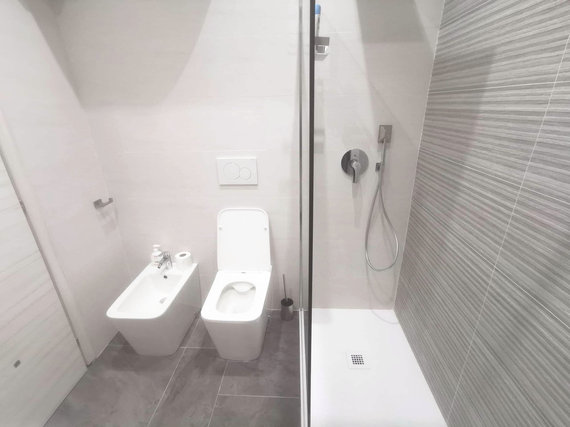 Panoramica del bagno privato con lavabo bianco, doccia e piastrelle grigie