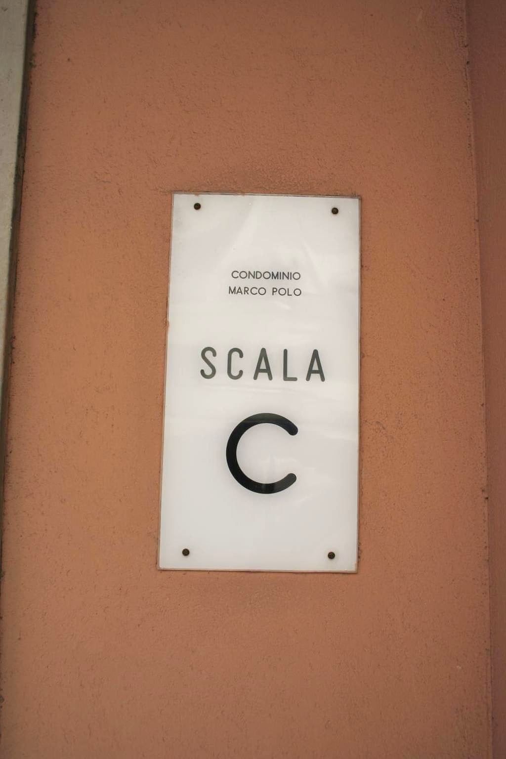Targa «Condominio Marco Polo, Scala C» su un muro color terracotta